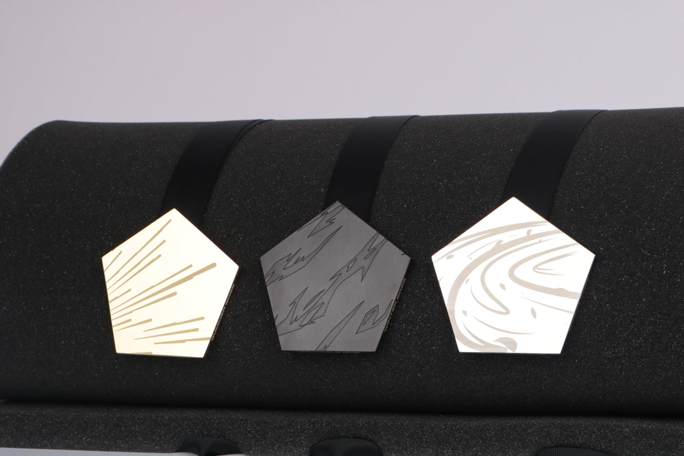 three medals on a black backdrop in chrome and anodized finish with etched text and graphics