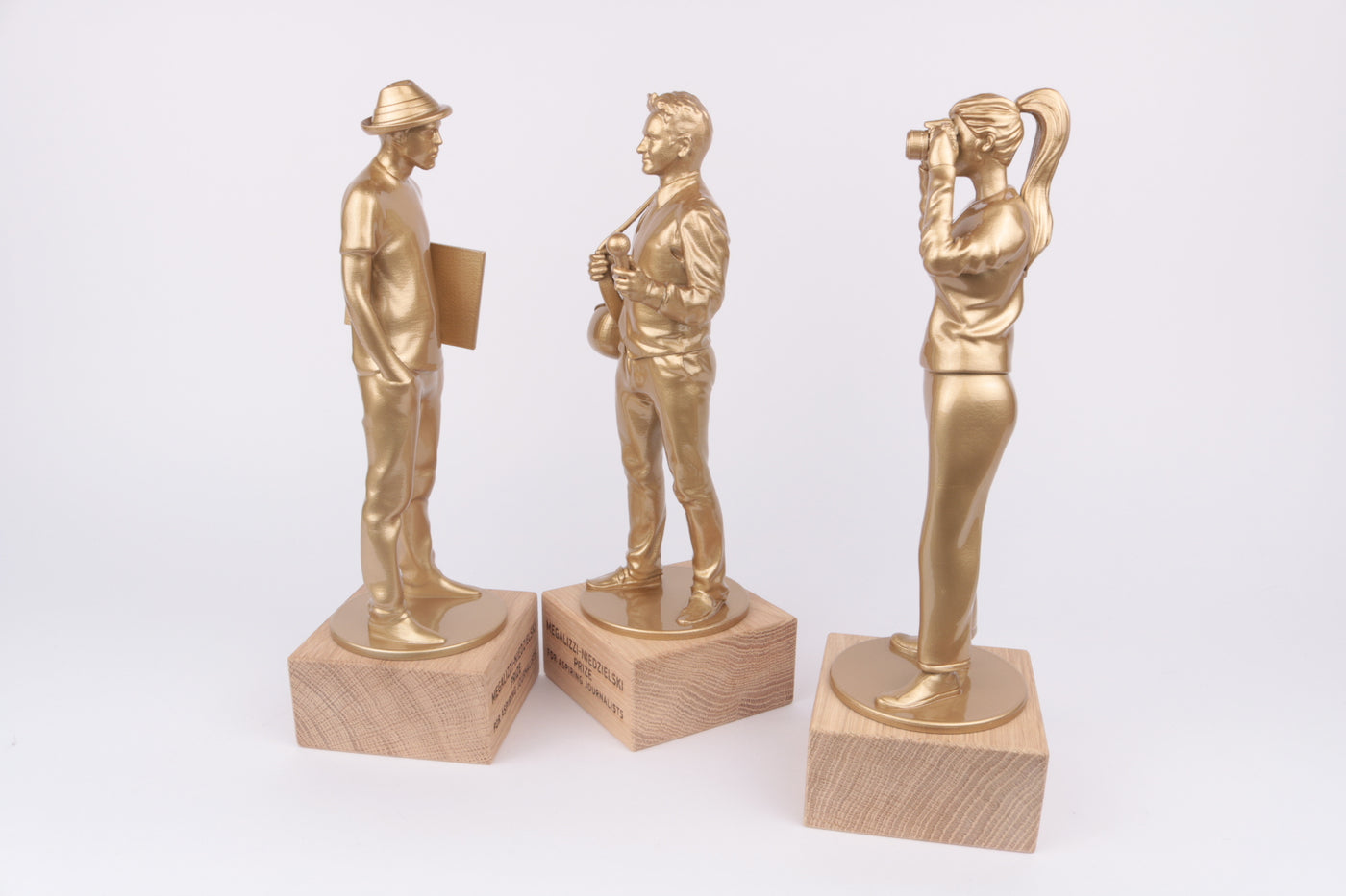 three journalist figurines finished in glossy gold metallic paint on oak base