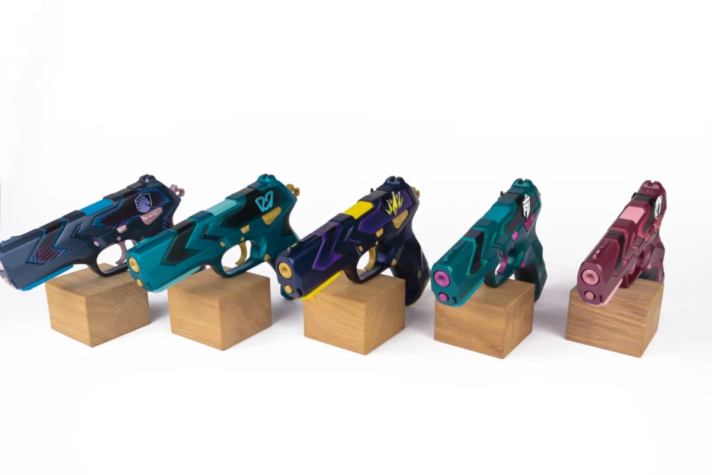 Five hand-painted Valorant Classic pistol replicas for VCT EMEA partner teams on oak blocks, produced by Fabit for Riot Games